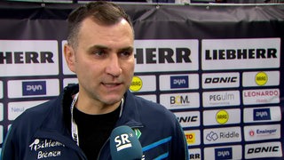 Werders Tischtennis-Trainer Cristian Tamas steht nach dem Aus im Pokal-Halbfinale beim Interview vor einer Werbewand.