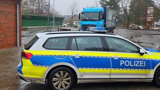 Ein Lkw und ein Polizeiauto stehen auf einem Parkplatz.