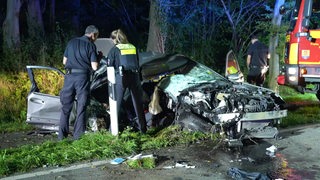 Ein komplett zertrümmertes Auto steht neben der Straße, davor stehen zwei Polizisten.