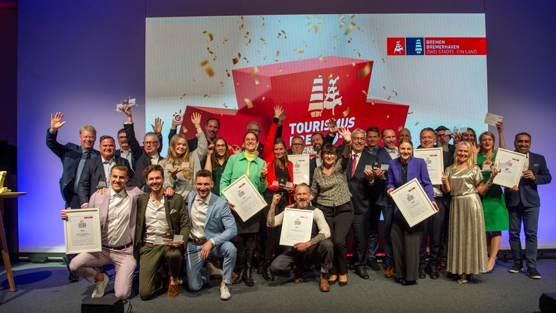 Auf einem Gruppenbild stehen Menschen zusammen und winken in die Kamera.