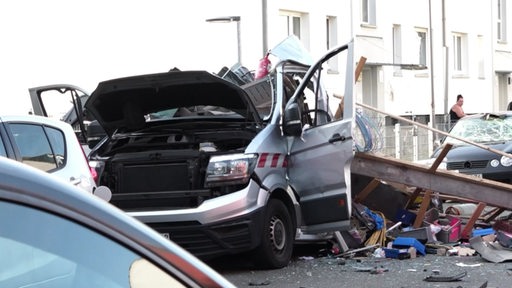 Ein zerstörter Transporter steht auf einer Straße. Daneben ist Gerümpel zu sehen