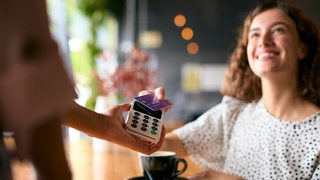 Eine junge Frau bezahlt in einem Café mit einer Visa-Karte.