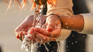 Eine Frau schöpft mit ihren Händen Trinkwasser aus einem Brunnen.