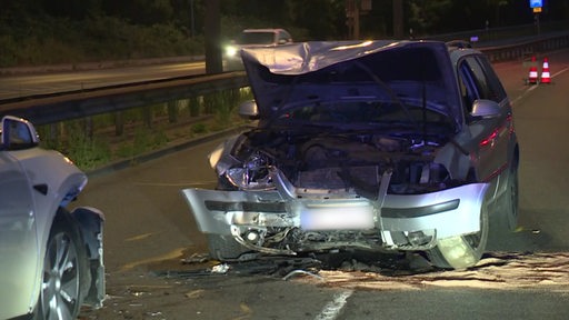 Ein stark beschädigter PKW steht im Dunkeln auf einer Straße.