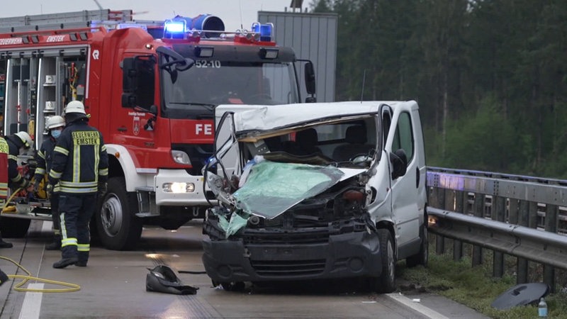 Eine Feuerwehrlaster und mehrere Einsatzkräfte stehen an einem Unfallwagen