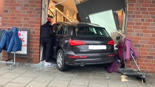 Ein Auto steht zwischen Kleiderständern und Scherben in einem Schaufenster.