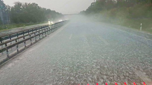 Blick auf eine Autobahn, auf die zahlreiche Hagelkörner fallen.