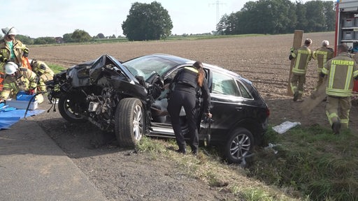 Einsatzkräfte von Polizei und Feuerwehr arbeiten neben einem Autowrack