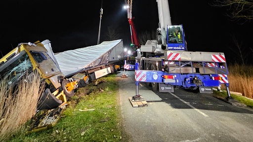 Ein Lkw liegt in einem Straßengraben und wird von einem Kran geborgen.