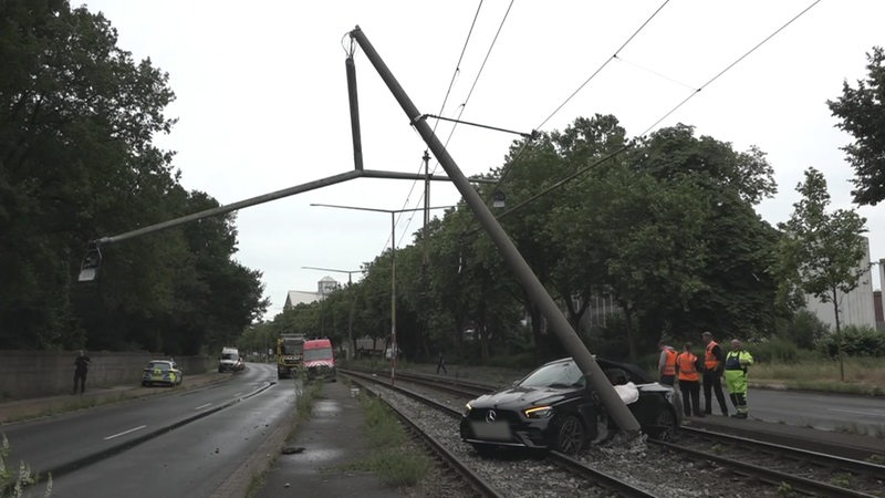 Ein Auto steht auf Gleisen neben einem umgeknickten Mast. 