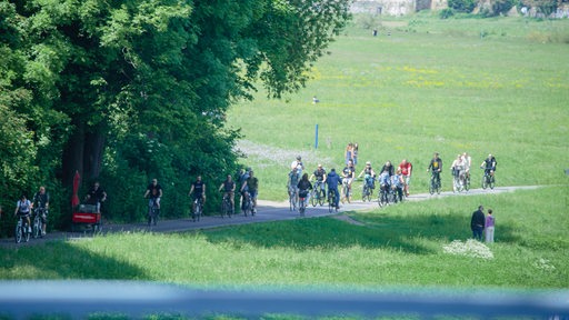 Auf einem Weg durch eine Wiese fahren Menschen mit Fahrrädern.