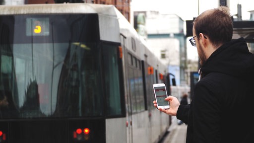 Ein Mann nutzt an einer Straßenbahnhaltestelle in Bremen die VBN "Fahrplaner"-App.