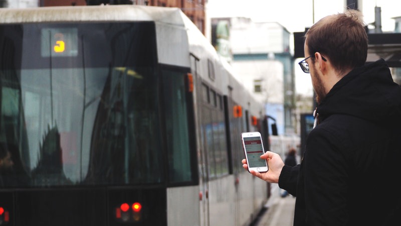 Ein Mann nutzt an einer Straßenbahnhaltestelle in Bremen die VBN "Fahrplaner"-App.