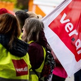 Streikende in Warnwesten halten eine Verdi-Fahne hoch.