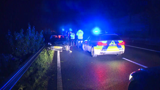 Mehrere Einsatzkräfte der Polizei stehen auf der Autobahn neben einem beschädigten Auto.