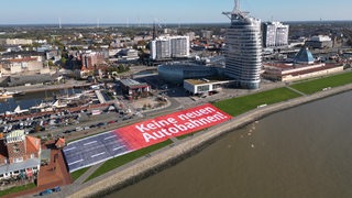 Eine Luftaufnahme zeigt ein Plakat auf einem Deich vor einer Skyline.