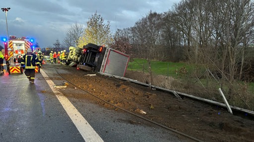 Ein LKW liegt umgekippt an der Autobahn. Rettungskräfte und Polizei sind im Einsatz