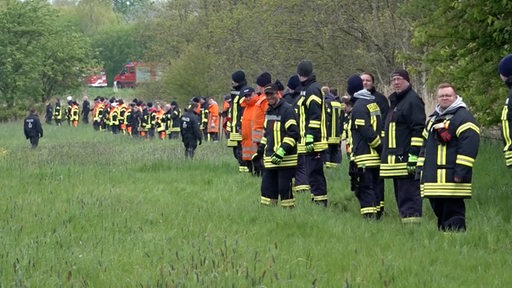 Etliche Einsatzkräfte stehen auf einem Feld.