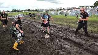 Fans stehen in Wackem im Schlamm und spielen Fußball