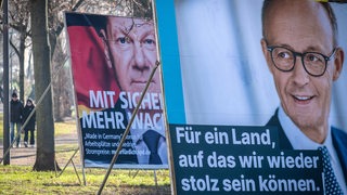 Ein Wahlplakat mit dem Gesicht von Friedrich Merz (CDU) steht vor einem mit Olaf Scholz (SPD).