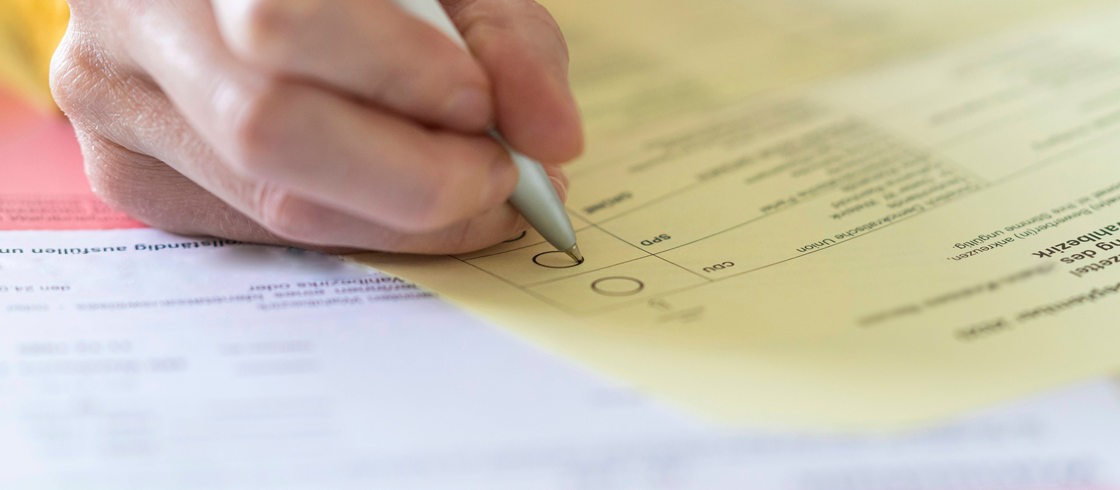 Nahaufnahme einer Hand mit Stift beim Ausfüllen des Wahlzettels