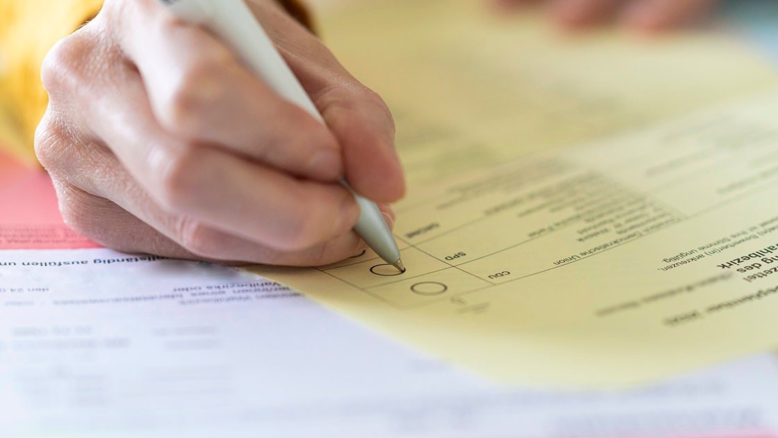 Nahaufnahme einer Hand mit Stift beim Ausfüllen des Wahlzettels