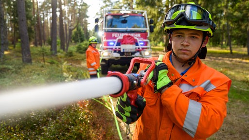 Ein Feuerwehrmann löscht mit einem Schlauch in einem Waldstück