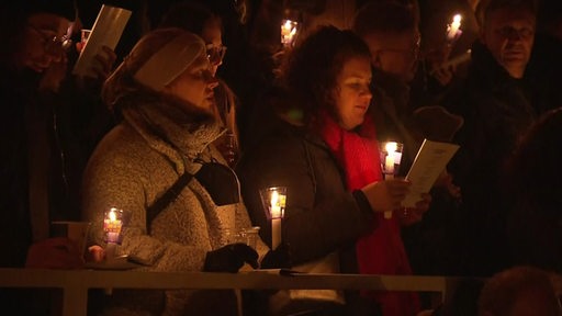 Singende Menschen im Chor mit Kerzen in der Hand. 