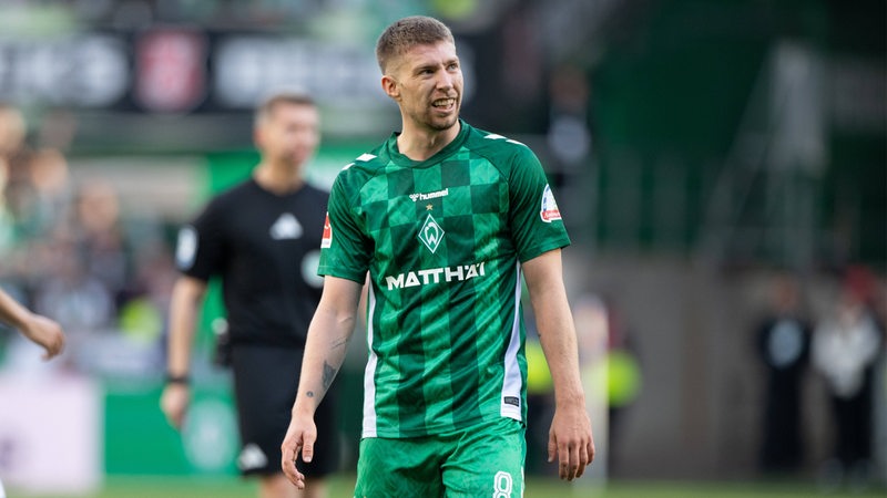 Ein Mann, Weiser, im Werder-Trikot steht auf dem Platz.