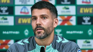 Anthony Jung von Werder Bremen sitzt bei einer Pressekonferenz auf dem Podium.