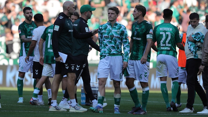 Werder-Spieler und Ole Werner stehen frustriert auf dem Rasen.