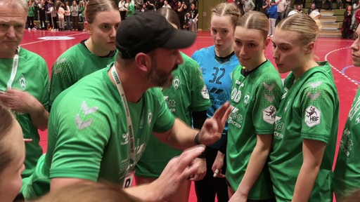 Der Trainer der Werder Frauen Handballmannschaft steht zwischen einigen Spielerinnen und gestikuliert