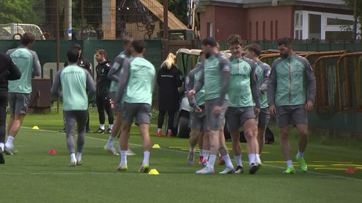 Eine Gruppe von Männern in Trainingskleidung, Werders Profifußballspieler, stehen auf dem Platz.