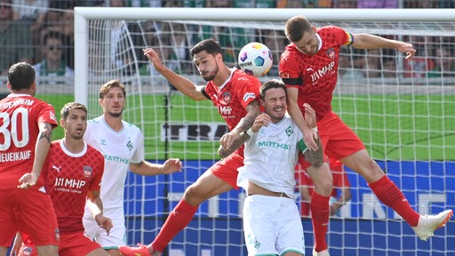 Zwei hochspringende Heidenheim-Spieler nehmen Werder-Verteidiger Marco Friedl in die Zange.