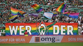 Werders Fans zeigen in der Ostkurve ein Transparent in Regenbogenfarben und schwenken Regenbogen-Fahnen