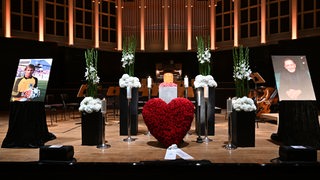 Auf der Bühne in der Glocke sind neben Blumen zwei Bilder von Dieter Burdenski zu sehen.