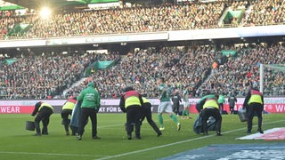 Ordner sammeln auf dem Rasen des Weser-Stadions Schokotaler ein.