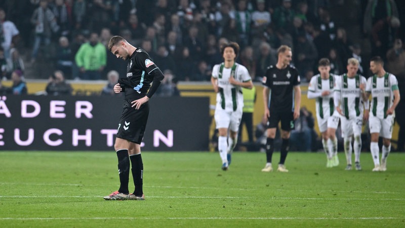 Marvin Ducksch schaut frustriert auf den Boden, als einige Gladbach-Spieler ein Tor bejubeln.