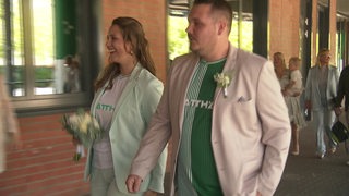 Eine Frau und ein Mann im Werder-Trikot und im Blazer und Sakko gehen nebeneinander mit einem Strauß