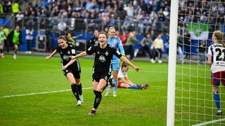 Fußballerinnen laufen sichtlich erfreut neben einem Tor.