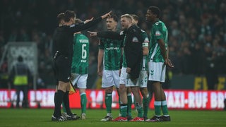 Mehrere Werder-Spieler diskutieren mit dem Schiedsrichter.