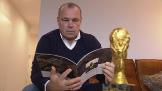 Andree Höttges, Sohn von Werder-Legende Horst-Dieter Höttges blättert in der Auktionsbroschüre, neben ihm die Replik des WM-Pokals.