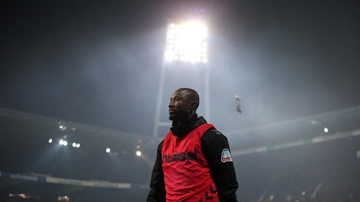 Naby Keita trägt im Weser-Stadion ein Trainingsleibchen. Über ihm scheint das Licht eines Flutlichtmasten.