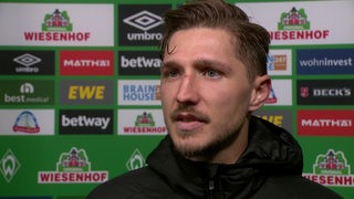 Werder-Verteidiger Niklas Stark beim Interview nach dem Spiel gegen Wolfsburg vor einer Werbewand.