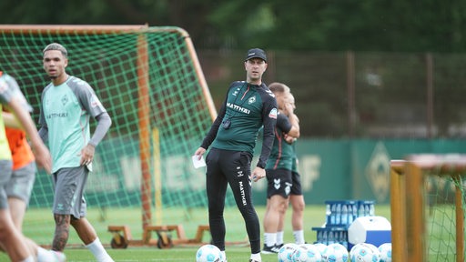 Werder Bremens Trainer Ole Werner steht auf dem Trainingsplatz und beugt sich mit dem Oberkörper zur Seite.