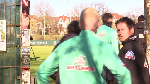 Ein Mann mit blondierten Haaren und Werder-Trainingskleidung betritt hinter der Mannschaft den Trainingsplatz.