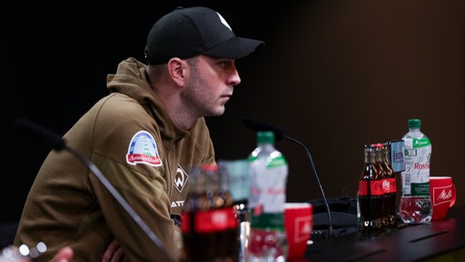 Ole Werner sitzt in dunkler Astmospähre auf dem Podium. 