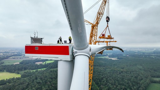 Arbeiter stehen auf der Plattform eines Windrades neben einem Kran.