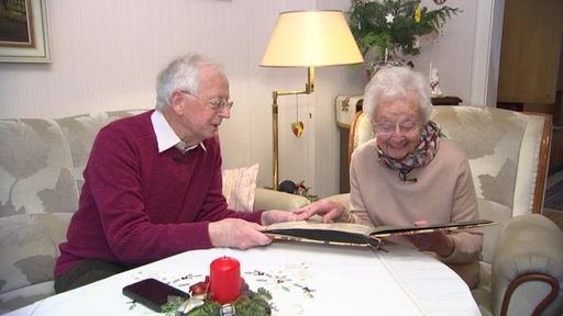 Zwei Senioren - ein Mann und eine Frau - sitzen im Wohnzimmer und blättert ein Fotoalbum