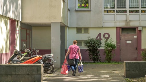 Eine Frau geht mit zwei Plastiktüten in den Eingang eines Sozialbaukomplexes